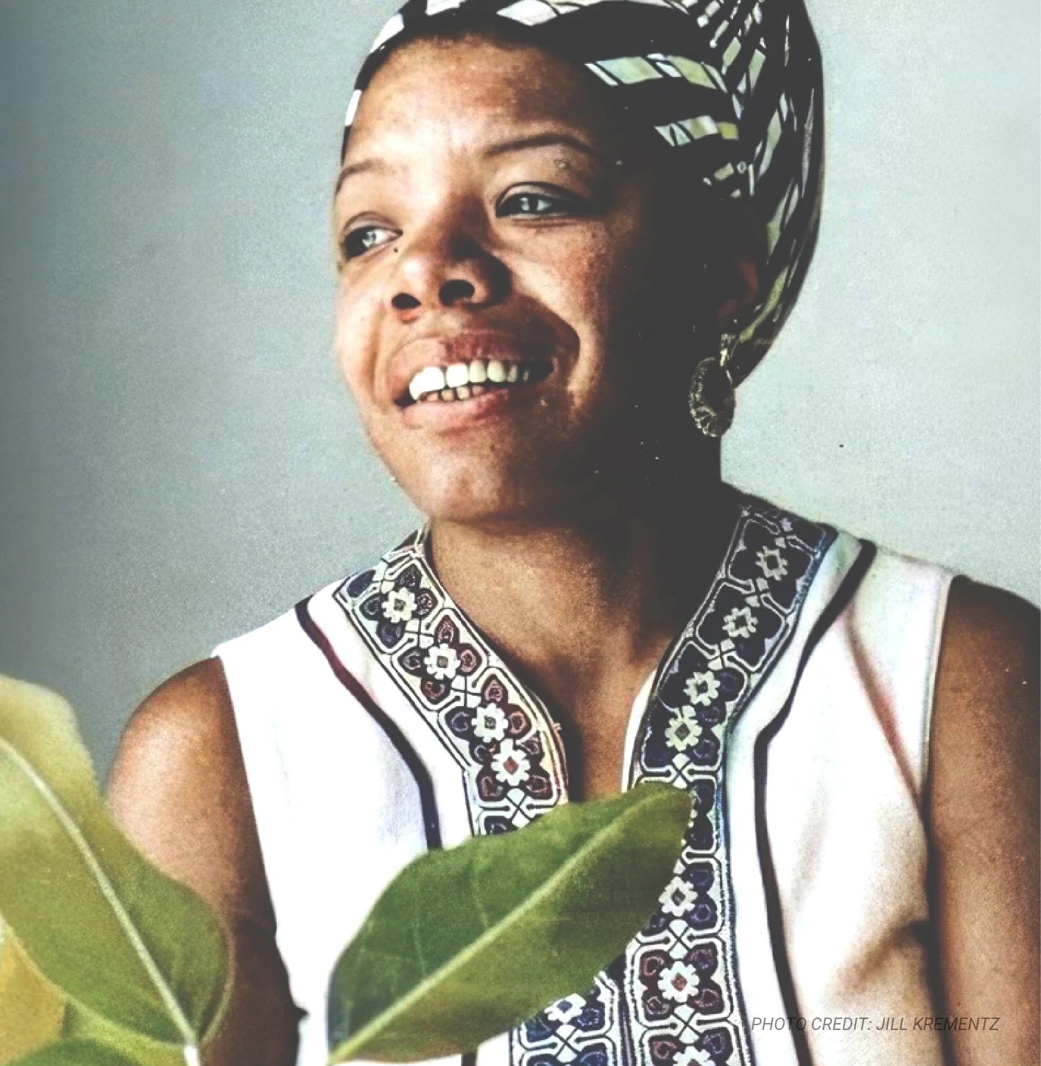 Maya Angelou wearing a patterned headscarf and top, holding green leaves against a plain background